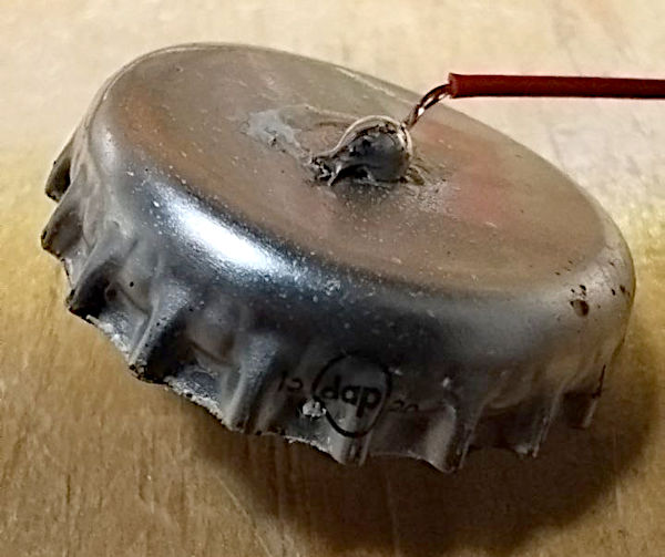 Un tappo corona di bottiglia con filo saldato Un tappo corona di bottiglia con filo saldato